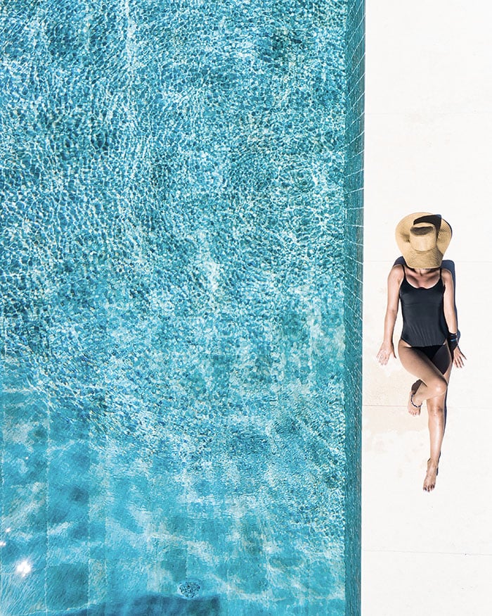 Woman in broad brimmed hat lounging at the edge of a pool